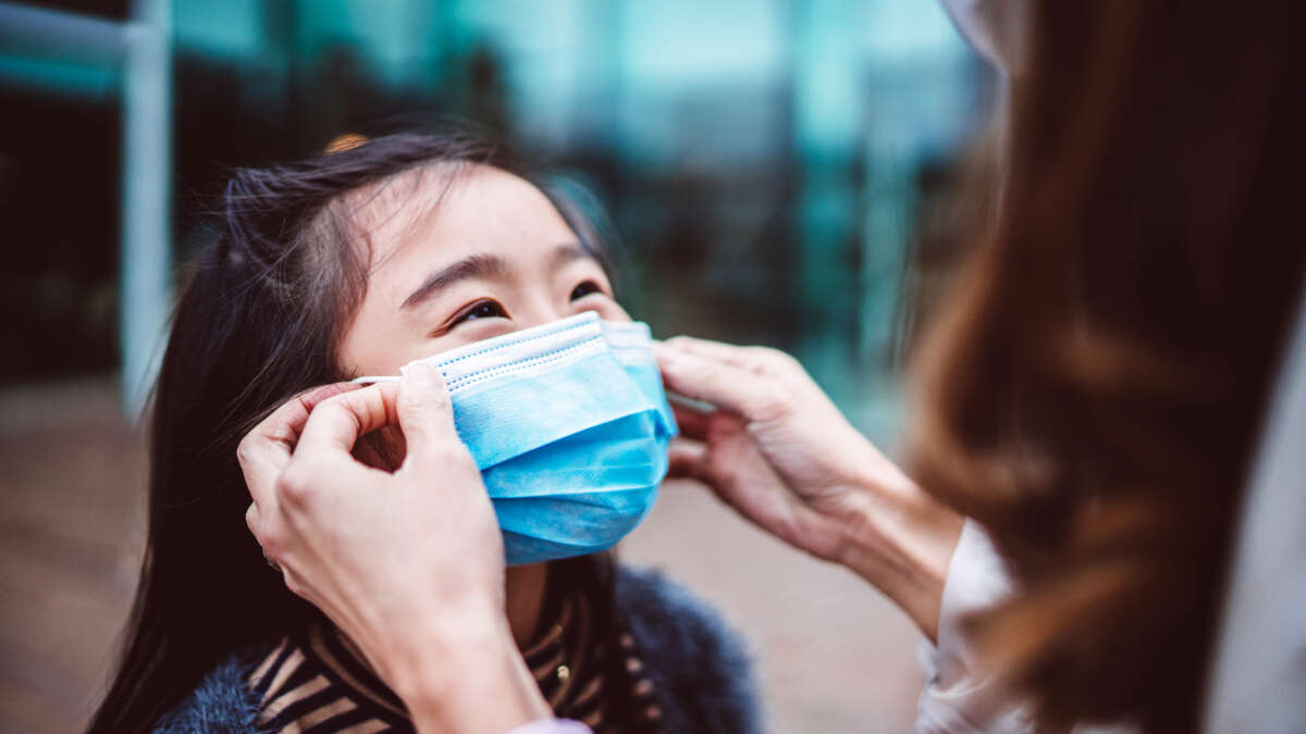 Mom helping her lovely daughter to wear medical face mask
