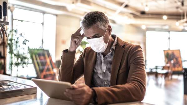 Mature businessman with mask using digital tablet at work